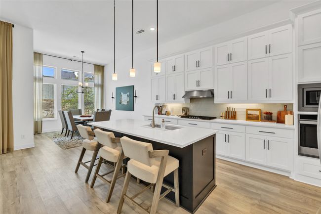 Kitchen featuring a sink, stainless steel appliances, under cabinet range hood, light wood finished floors, and tasteful backsplash | Image 14