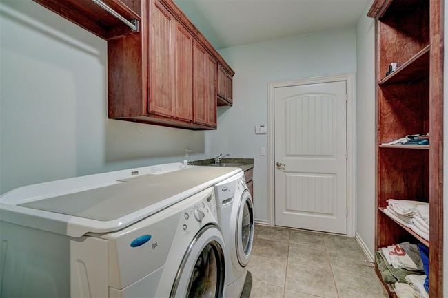 Clothes washing area featuring cabinet space, light tile patterned floors, a sink, and washer and clothes dryer | Image 39