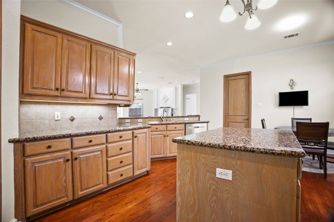 Kitchen with dark wood-style floors, a kitchen island, decorative backsplash, stone countertops, and ornamental molding | Image 8