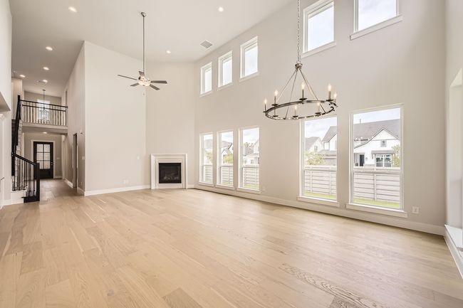 Unfurnished living room with a towering ceiling, a chandelier, light wood-type flooring, a fireplace, and recessed lighting | Image 9
