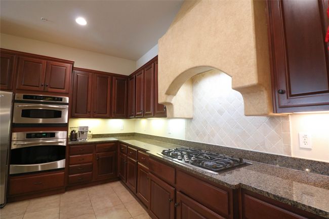 Kitchen with dark stone counters, tasteful backsplash, appliances with stainless steel finishes, light tile patterned flooring, and reddish brown cabinets | Image 11