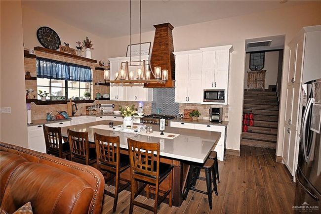 Kitchen featuring appliances with stainless steel finishes, decorative backsplash, white cabinets, dark wood-type flooring, and hanging light fixtures | Image 8