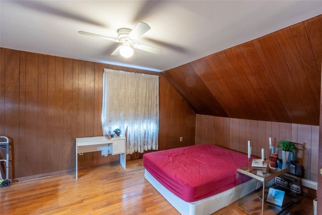 Bedroom featuring ceiling fan, lofted ceiling, wood walls, and wood finished floors | Image 19