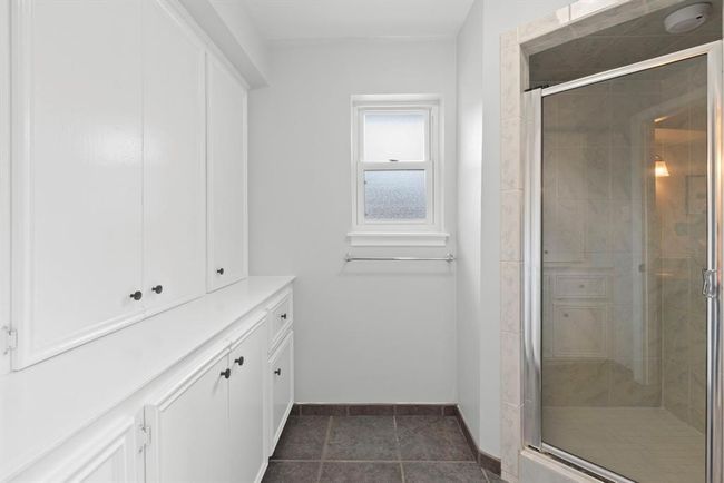 The primary bathroom also features ample white cabinetry for storage, a window for natural light, a glass-enclosed shower, and tiled flooring. | Image 21