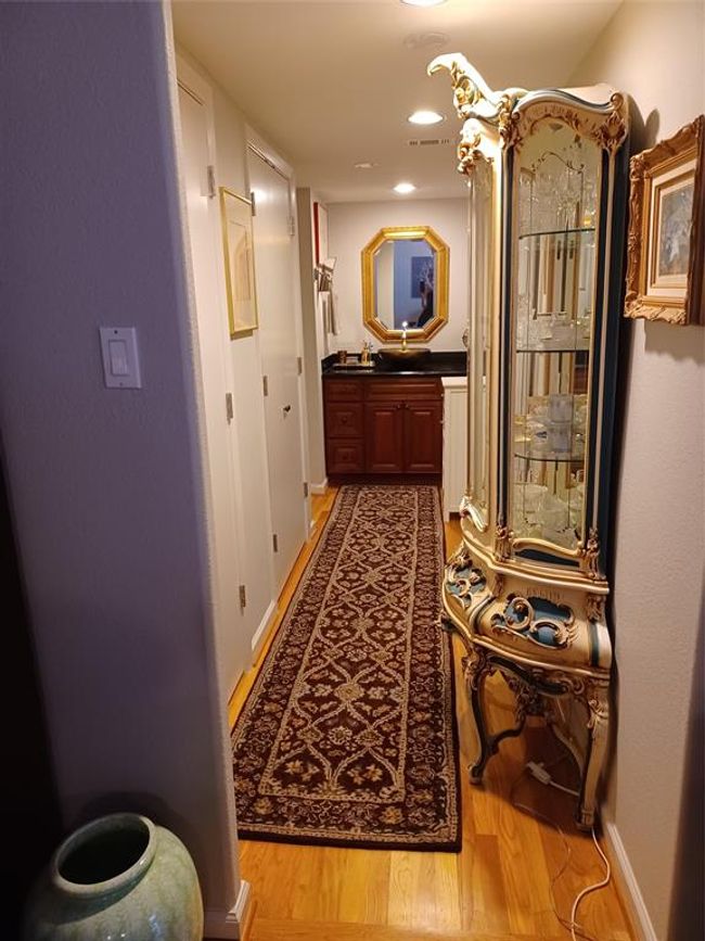 Looking down the hallway while leaving the living room. There is a double storage closet on the left with shelving inside the furthest closet from this point of view. The vanity is outside of the water closet area. | Image 14