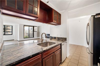 Kitchen with dark stone countertops, a textured ceiling, light tile patterned floors, sink, and appliances with stainless steel finishes | Image 1