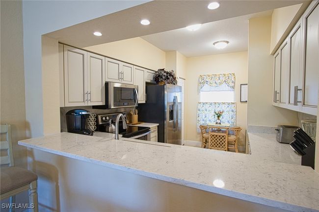 Kitchen with appliances with stainless steel finishes, white cabinets, kitchen peninsula, light stone counters, and a kitchen bar | Image 11