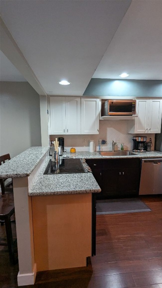 Kitchen with stainless steel dishwasher, a sink, dark wood finished floors, electric cooktop, and white cabinetry | Image 10