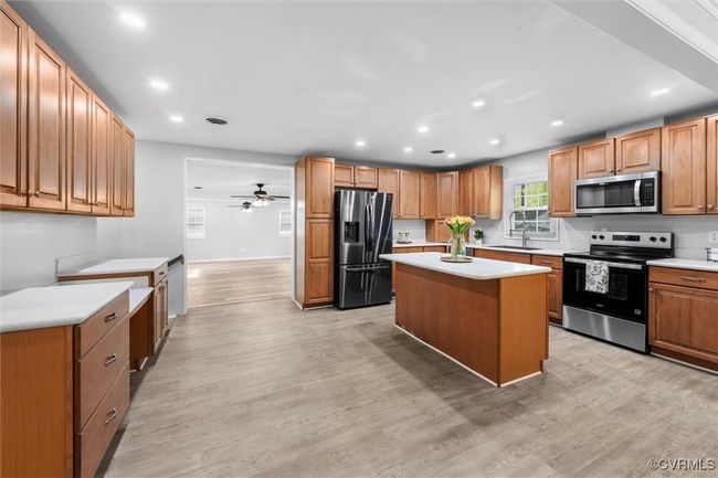 Kitchen with light wood-style flooring, stainless steel appliances, light countertops, a kitchen island, and a sink | Image 10