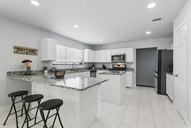 Kitchen with appliances with stainless steel finishes, a peninsula, recessed lighting, light stone counters, and a breakfast bar | Image 6