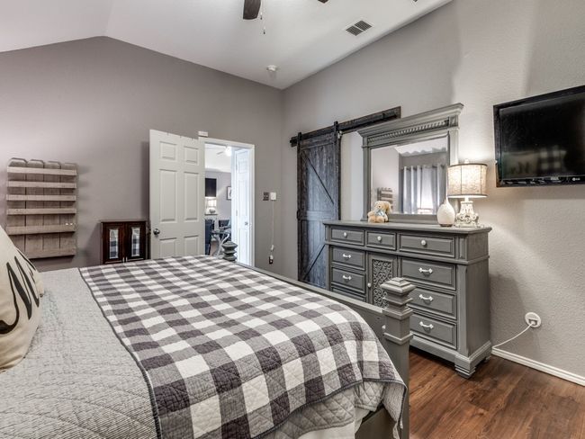 Bedroom featuring dark wood-style flooring, vaulted ceiling, a barn door, baseboards, and ceiling fan | Image 17