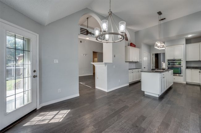 Kitchen featuring high vaulted ceiling, dark countertops, a chandelier, appliances with stainless steel finishes, and white cabinetry | Image 12