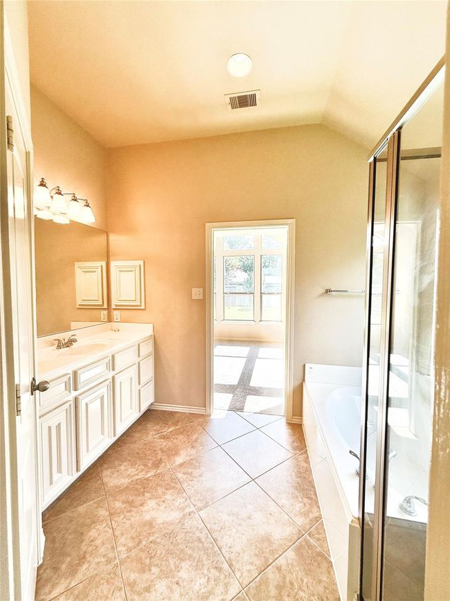 This bright bathroom features a large soaking tub, separate glass-enclosed shower, dual-sink vanity with ample storage, and stylish tile flooring. A window offers plenty of natural light, creating an inviting and relaxing atmosphere. | Image 17
