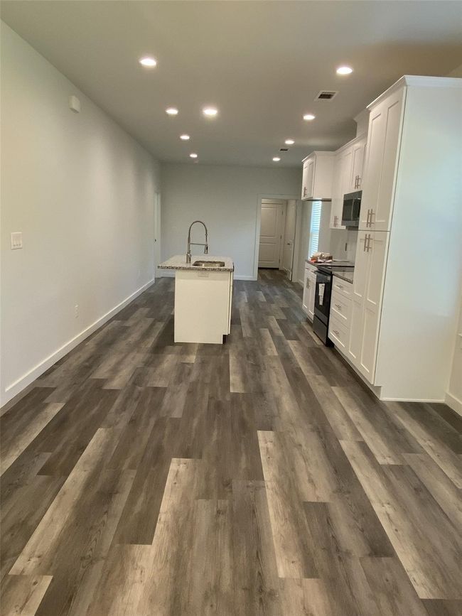 Kitchen with black electric range oven, stainless steel microwave, baseboards, white cabinetry, and an island with sink | Image 4