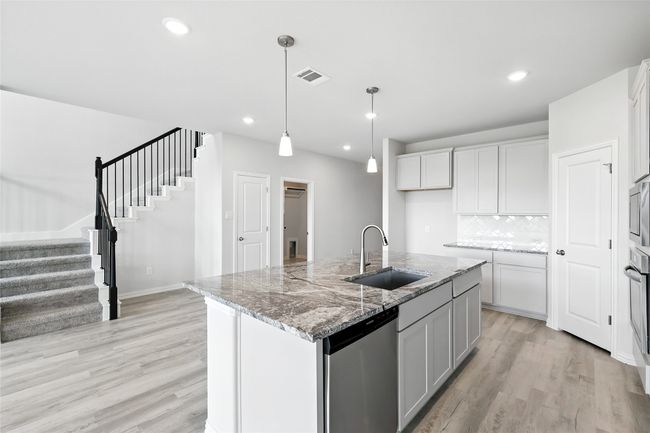 Kitchen featuring stainless steel appliances, light wood-style flooring, backsplash, decorative light fixtures, and light stone countertops | Image 4