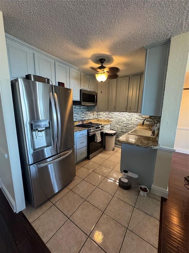 Kitchen with appliances with stainless steel finishes, backsplash, a ceiling fan, a textured ceiling, and light tile patterned floors | Image 4