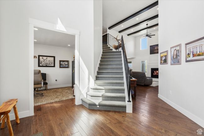 Stairs featuring a high ceiling, wood-type flooring, a ceiling fan, and a warm lit fireplace | Image 6