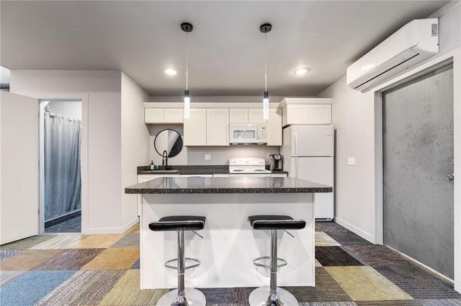 Kitchen featuring white appliances, white cabinetry, a kitchen island, and a wall mounted air conditioner | Image 15