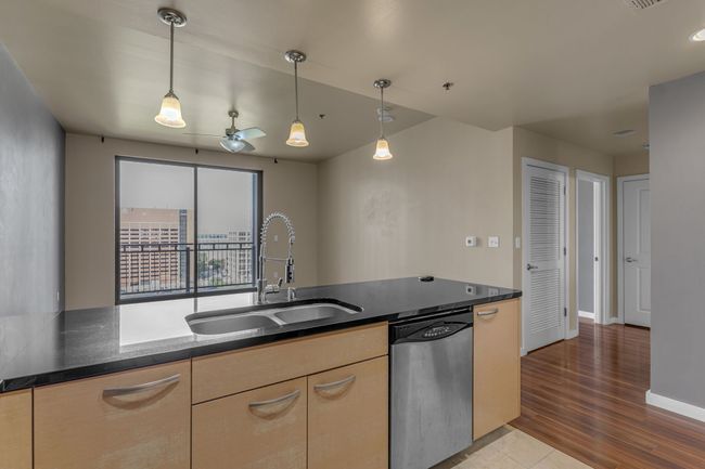 Kitchen featuring dark stone countertops, pendant lighting, stainless steel dishwasher, and a sink | Image 7