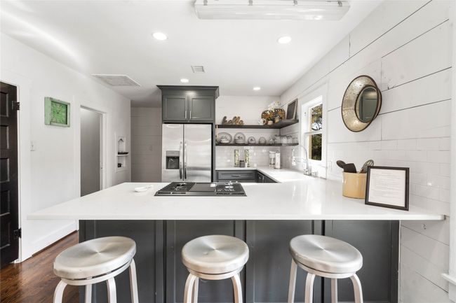Kitchen with stainless steel fridge with ice dispenser, open shelves, gas cooktop, light countertops, and dark wood-style floors | Image 12
