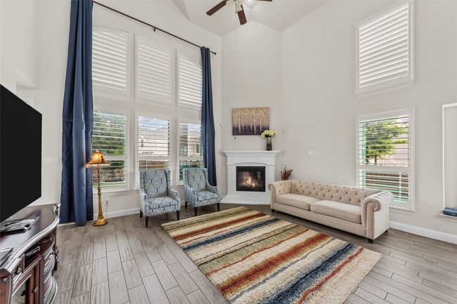 Living area featuring high vaulted ceiling, a ceiling fan, a glass covered fireplace, wood finished floors, and baseboards | Image 16