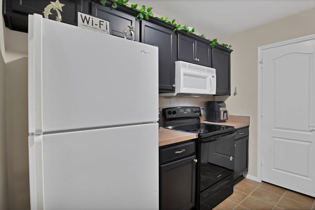 Kitchen featuring decorative backsplash, dark cabinets, butcher block countertops, white appliances, and tile patterned​​‌​​​​‌​​‌‌​‌‌​​​‌‌​​‌‌​‌​​​​​‌ flooring | Image 13