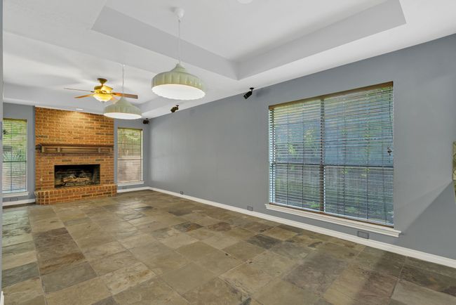 Unfurnished living room featuring a tray ceiling, stone tile flooring, a ceiling fan, and a fireplace | Image 12