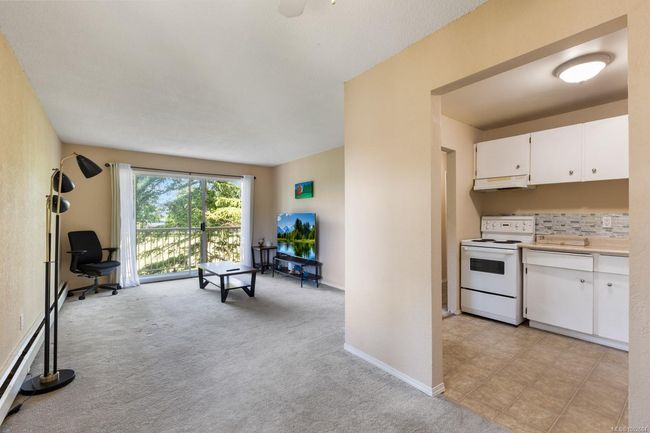 Kitchen featuring white electric stove, white cabinetry, light countertops, under cabinet range hood, and light carpet | Image 12