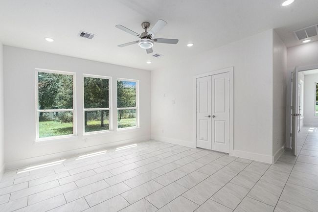 Bright, spacious room with large windows offering a view of greenery. Features modern tile flooring, a ceiling fan, and double doors, ideal for flexible use. | Image 29