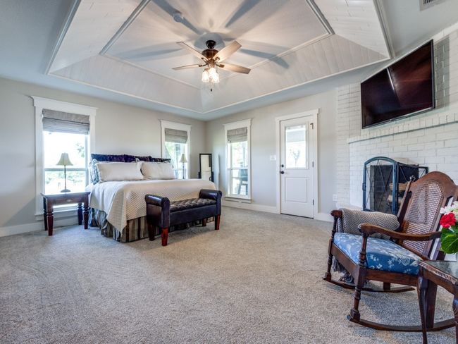 Oversized primary bedroom retreat is on the opposite side of the home from all the guest bedrooms. With a cozy fireplace, ensuite bath, beautiful property views, and access to the back porch, this room is the perfect place to wind down at the end of a day. | Image 14