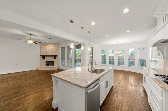 Kitchen featuring a stone fireplace, a sink, white cabinetry, and dishwasher | Image 8