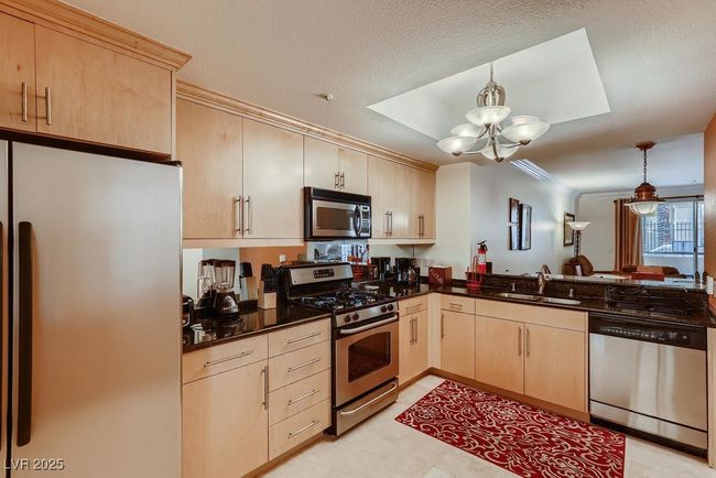Kitchen featuring stainless steel appliances, light brown cabinets, a chandelier, decorative light fixtures, and a peninsula | Image 25
