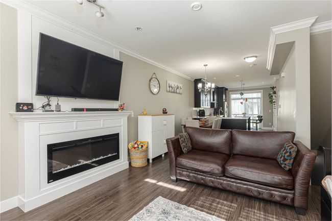 Living room featuring wood finished floors, ornamental molding, a chandelier, and a glass covered fireplace | Image 7