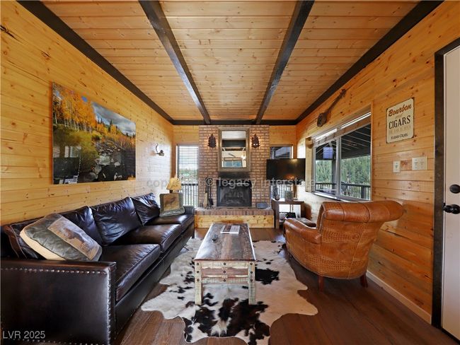 Living area featuring a brick fireplace, hardwood / wood-style floors, wooden walls, wooden ceiling, and lofted ceiling with beams | Image 7