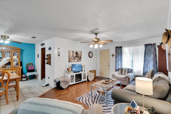 Living area with ceiling fan, a textured ceiling, and light tile patterned floors | Image 5