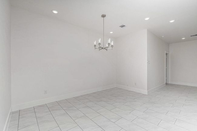 This room features a modern, open layout with light tile flooring and recessed lighting. It's complemented by a stylish chandelier, offering a bright and spacious feel, perfect for dining or living space. | Image 18