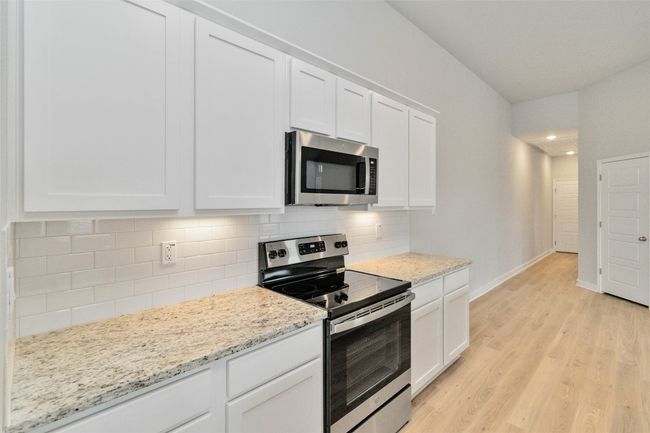 Kitchen with tasteful backsplash, appliances with stainless steel finishes, white cabinetry, light wood-type flooring, and baseboards | Image 18