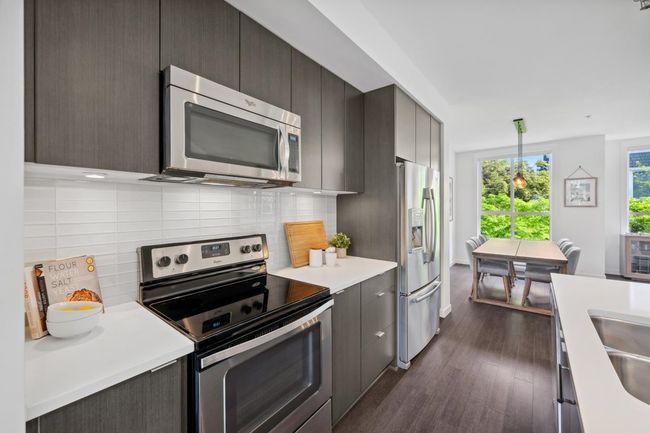 Kitchen with stainless steel appliances, light countertops, dark wood finished floors, backsplash, and decorative light fixtures | Image 10