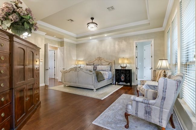 Primary Bedroom featuring a tray ceiling, dark wood floors, crown molding, and generous space for a sitting area. | Image 14