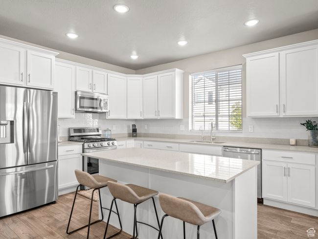 Kitchen featuring stainless steel appliances, a breakfast bar area, white cabinetry, light wood-style flooring, and recessed lighting | Image 12