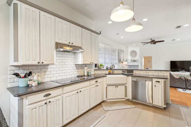 Kitchen with a peninsula, dishwasher, dark countertops, under cabinet range hood, and black electric stovetop | Image 11