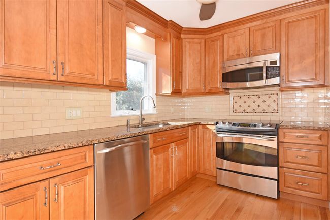 Kitchen featuring a sink, light wood-style floors, appliances with stainless steel finishes, decorative backsplash, and light stone countertops | Image 11