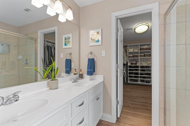 Bathroom with double vanity, a walk in closet, a stall shower, and wood finished floors | Image 16
