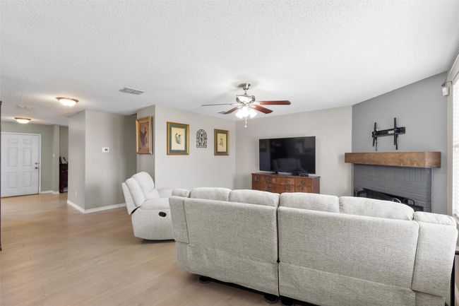 Living area featuring ceiling fan, light wood-style floors, a textured ceiling, and a brick fireplace | Image 7