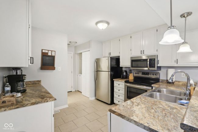 kitchen featuring stainless steel appliances, a sink, light tile patterned flooring, white cabinetry, and hanging light fixtures | Image 10