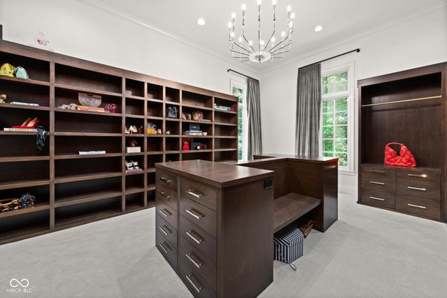 primary closet, walk in closet featuring light colored carpet and a chandelier | Image 35