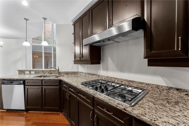 Kitchen featuring stainless steel appliances, light wood-style flooring, a sink, dark brown cabinetry, and under cabinet range hood | Image 9