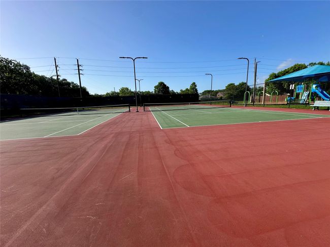 This photo shows a well-maintained tennis court with surrounding fencing and nearby playground equipment, ideal for outdoor recreation in a residential setting. | Image 20