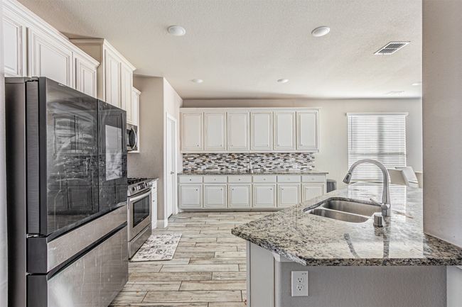 Kitchen featuring appliances with stainless steel finishes, a sink, light wood-style floors, light stone counters, and white cabinets | Image 10