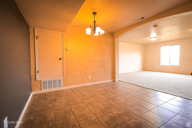 Carpeted spare room featuring arched walkways, tile patterned flooring, a textured ceiling, and a chandelier | Image 23